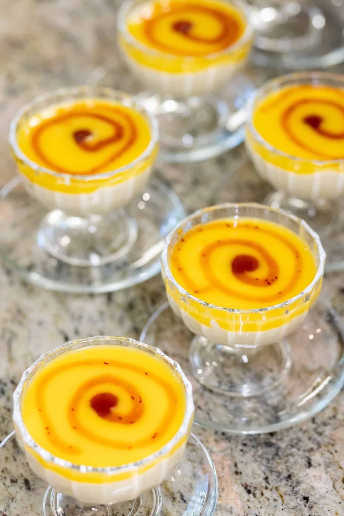 Mango-Pudding in Gläsern mit dekorativem Muster, serviert auf Marmoroberfläche.
