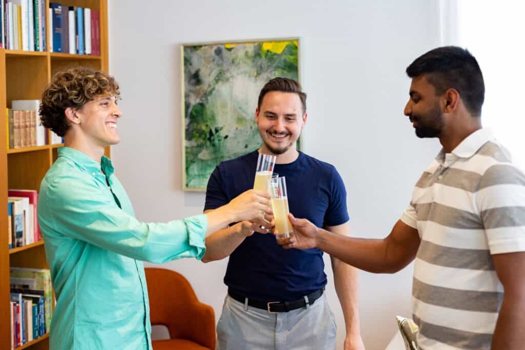 Drei Studenten stoßen mit Getränken im Gemeinschaftsraum des Studentenhauses Sillgraben an.