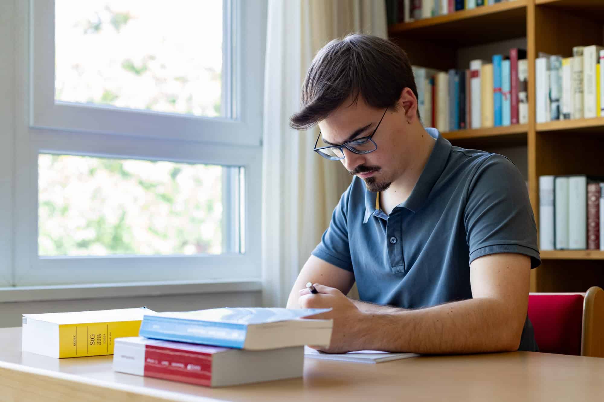 Junge Person studiert in einem hellen Raum mit Büchern im Hintergrund.