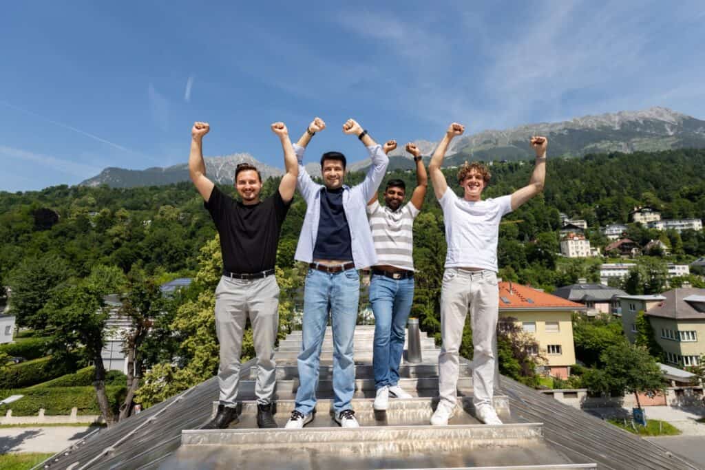 Vier junge Menschen feiern auf einem Dach mit Bergblick im Hintergrund.